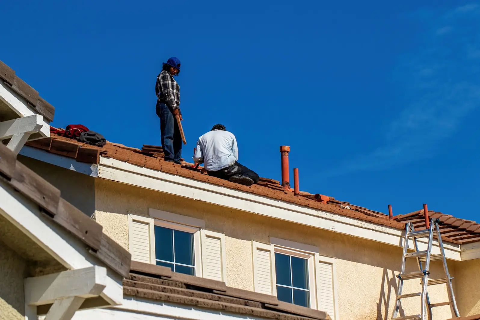 Deux couvreurs au travail sur la toiture d'une maison, échelle posée en façade
