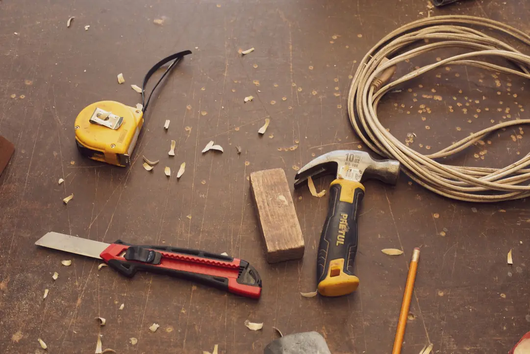 Outils de chantier posés sur un établi : mètre, cutter, marteau et cordeau